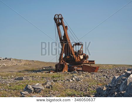 An Old Rusty Broken Excavator Stands Against The Background Of Stones