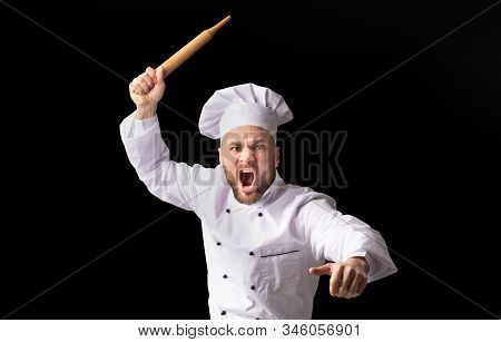 Angry Chef Bakerman Raising Rolling Pin Threateningly Posing Over Black Background. Studio Shot