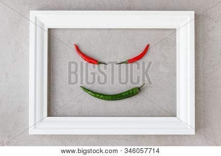 Creative Image Of Devil Smile Crated Of Hot Red And Green Chilli Peppers In White Frame On Concrete 