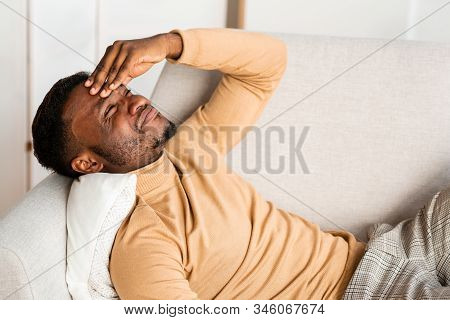 Headache. African American Man Having Migraine Touching Forehead Suffering From Pain Lying On Couch 