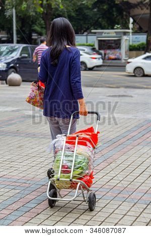 Shenzhen, China - November 24 2018: Woman Carrying Groceries In Shopping Cart Full Of Throw-away Pla