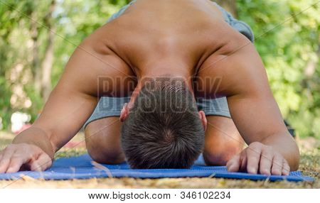 Young Athletic Sunburnt Man In Balasana Yoga Pose On A Blue Mat