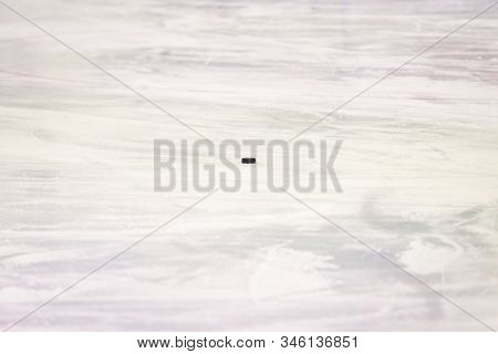 Black Ice Hocikey Rubber Puck Located On Arena Ice Rink. Ice And Puck Have Small And Deep Scratches.