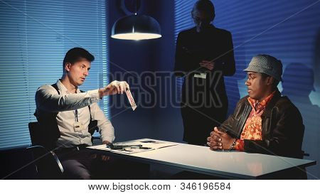 Medium Shot Of Detective Showing Picture Of Suspected Robbers Accomplice During Interview In Police 
