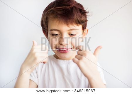 Horizontal Portrait Of 7 Years Old Smiling Child In White T-shirt Looking On Dental Floss For Teeth 