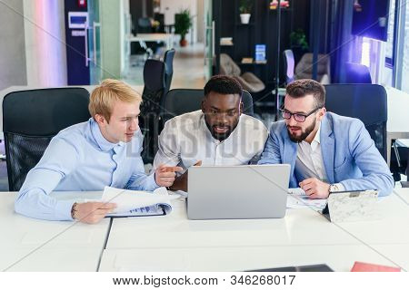 Businessmen Sitting At The Office Table And Comparing Data From Report And Computer To Succeed In Co