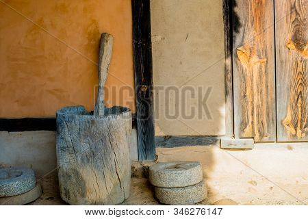 Wooden Mortar And Pestle In Front Of Wall Of Stucco Building In Public Park.