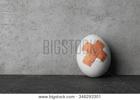 Cracked Egg With Sticking Plasters On Grey Stone Table, Space For Text