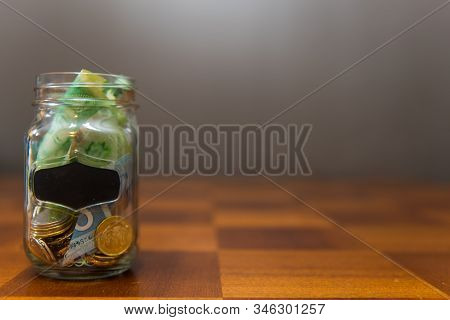 Transparent Glass Jar With Money Inside On Top Of Wooden Table.  Concept For Swear Jar, Savings, Bud