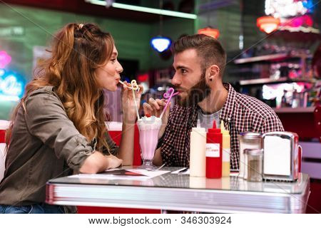 Image of a happy young loving couple sit in retro bright cafe drinking cockail indoors.