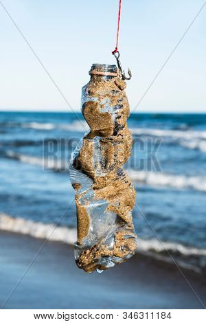 closeup of a used plastic bottle, covered with wet sand, in a fish hook, freshly fished in the ocean