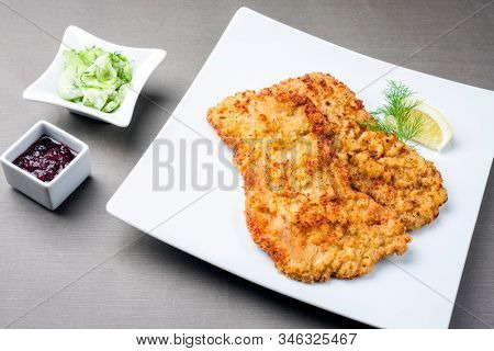 Traditional deep fried Wiener schnitzel from veal topside with cucumber salad and cranberry jam offered as closeup on a modern design plate on a rustic wooden board 