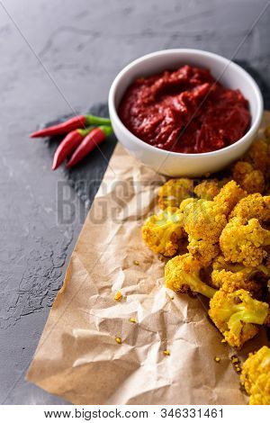 Vertical Image Of Cauliflower In Batter On Craft Paper With Chili Sauce On Dark Background With Copy