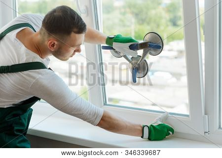 Young Worker Is Repairing Window, Holding A Pane With A Vacuum Lifter
