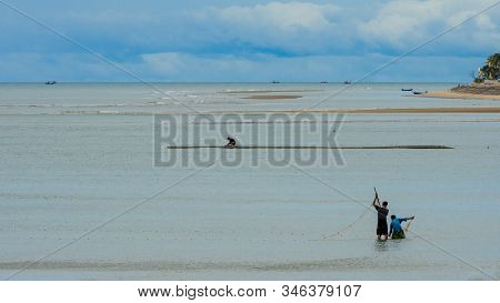 Two Fishermen Standing In The Water At Low Tide Fisihing With A Net At Beach In Pak Nam Pran, Pranbu