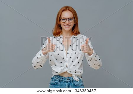 Cheerful Beautiful Young Redhead Woman Shows Thumbs Up, Likes Amazing Idea, Gives Positive Feedback 