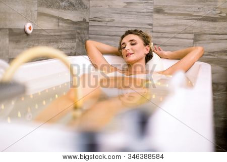 Young Smiling Pretty Woman In Modern Bathtub During Hydromassage In Beauty Salon