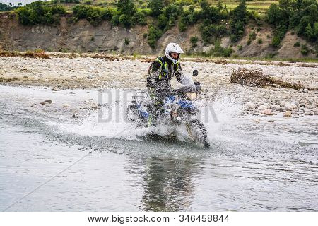 Gramsh, Albania - July 30, 2019. Moto Biker Crossing The River With Splashing Water