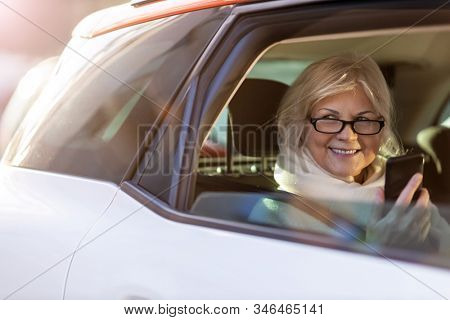Senior woman with smartphone on the back seat of a car
