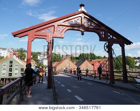 Trondheim, Norway On July 2019: Wooden Town Bridge Over Nidelva River And Colorful Houses In Backgro