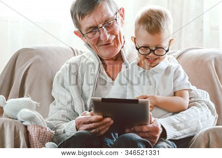 Elderly Grandfather And His Little Grandson Use A Tablet Device