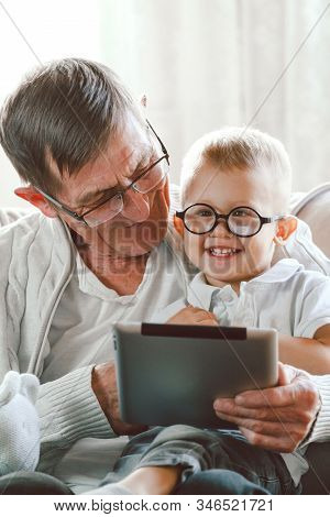 Elderly Grandfather And His Little Grandson Use A Tablet Device