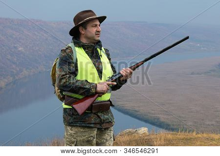 Hunter Man In Camouflage With A Gun During The Hunt In Search Of Wild Birds Or Game. Autumn Hunting 