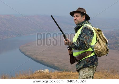 Hunter Man In Camouflage With A Gun During The Hunt In Search Of Wild Birds Or Game. Autumn Hunting 