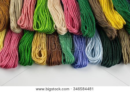 At The Top Of The Photo, Embroidery Threads Lie Vertically. They Have Various Color Shades.