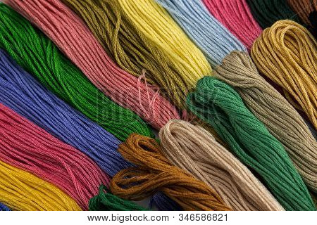 At The Top Of The Photo, Embroidery Threads Lie Vertically. They Have Various Color Shades.