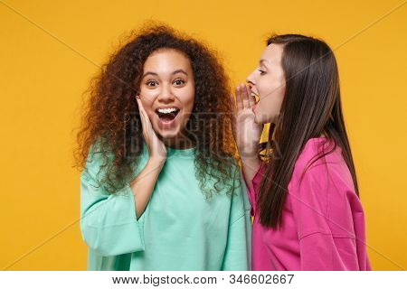Two Excited Women Friends European African American In Pink Green Clothes Isolated On Yellow Backgro