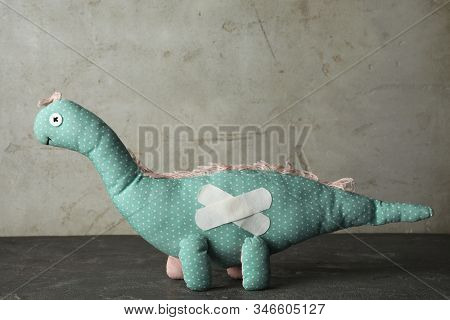 Toy Dinosaur With Sticking Plasters On Grey Stone Table