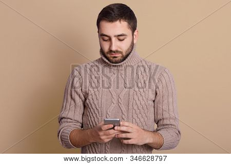 Close Upportrait Of Handsome Young Man Using His Smartphone While Standing Isolated Over Beige Backg