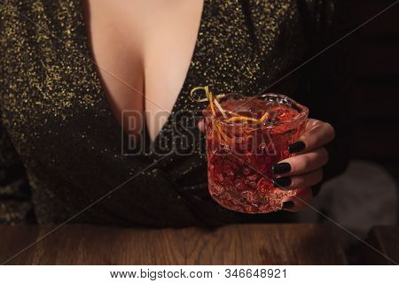 Girl In Evening Dress With Big Breast Holds An Alcohol Cocktail In A Hand. Hot Woman At The Party. T
