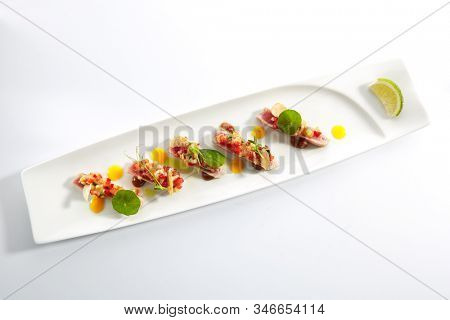 Appetizer with tuna tartar, seasonal vegetables and greens on white restaurant plate isolated. Macro photo of delicious healthy red fish tatar or tar-tar entree topview