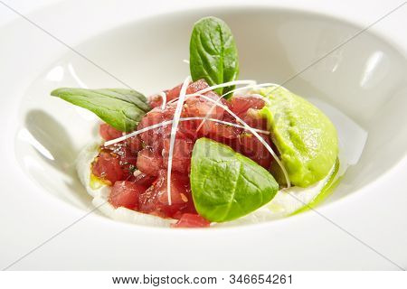 Gourmet tuna tartar with various dip and vegetables on white restaurant plate isolated. Macro shot of raw yellowfin fish tatar, luxury healthy food, seafood with cream sauce and spinach closeup