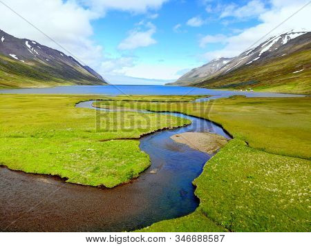 The Aerial View Of A Blue Creek Flowing Into The Lake Near Hedinsfjordur, Iceland