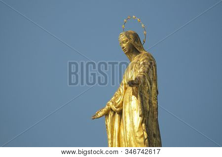 Close Up View Of The Golden Madonnina (madonna - Immacolata) Statue Against The Blue Sky Located At 
