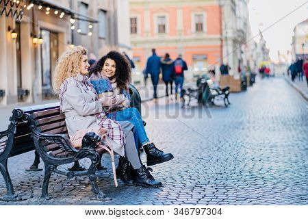 Full Hieght Of Two Multiethnic Mixed Race Curly Different Female Enjoying Winter Sunny Day, Sits On 