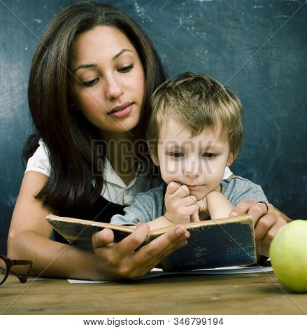 Little Cute Boy In Glasses With Young Real Teacher, Classroom Studying At Blackboard School Kido