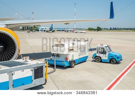 Big Modern Commercial Plane Parked On Airport Runway And Connected To Ground Supply Power Unit. Airc