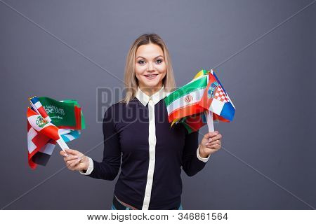 Cheerful Young Woman With A Large Set Of Flags Of Different Countries Of The World. Polyglot, And Le