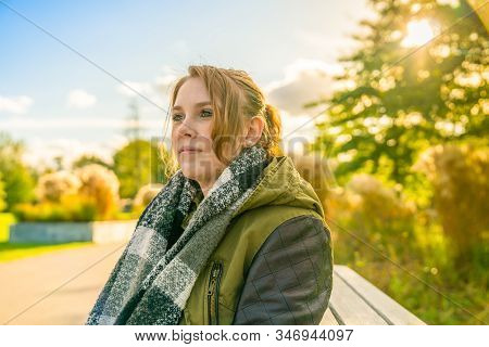 A Young Woman Sits Contentedly On A Parkbench In Autumn