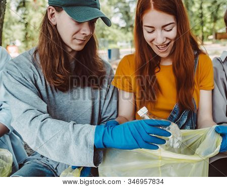 Man And Woman Picking Up Trash From The Park. They Collecting The Litter In Garbage Bag