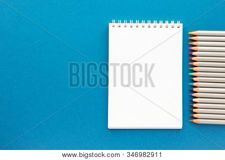 Blank Notepad On Spirals And Colorful Pencils On Bright Blue Background. Sketchbook For Drawing. Art