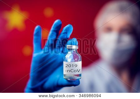 A Doctor In Blue Medical Gloves And Mask Holding An Ampula With Vaccine In Front Of Flag Of China. C