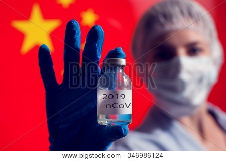 A Doctor In Blue Medical Gloves And Mask Holding An Ampula With Vaccine In Front Of Flag Of China. C
