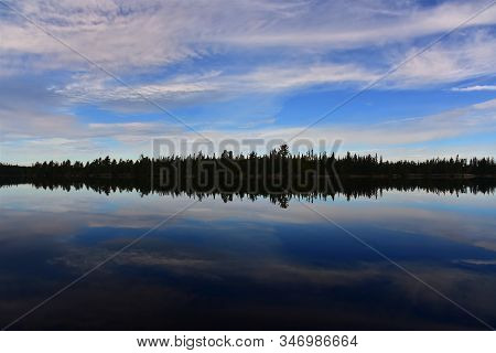Dramatic Mirrored Silhouette Of A Boreal Forest Tree Line And A Cloudy Blue Sky In Cirrus Lake, Quet