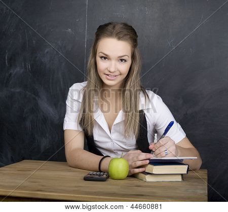 Ritratto di felice studente carino con calcolatrice, libro, penna e verde mela vicino a lavagna