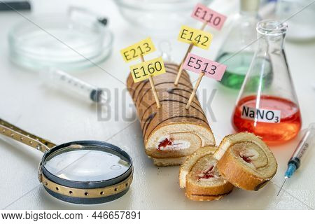Food Additives: Sweet Roll With Chemical Additives With Colored Labels, On A Laboratory Table.